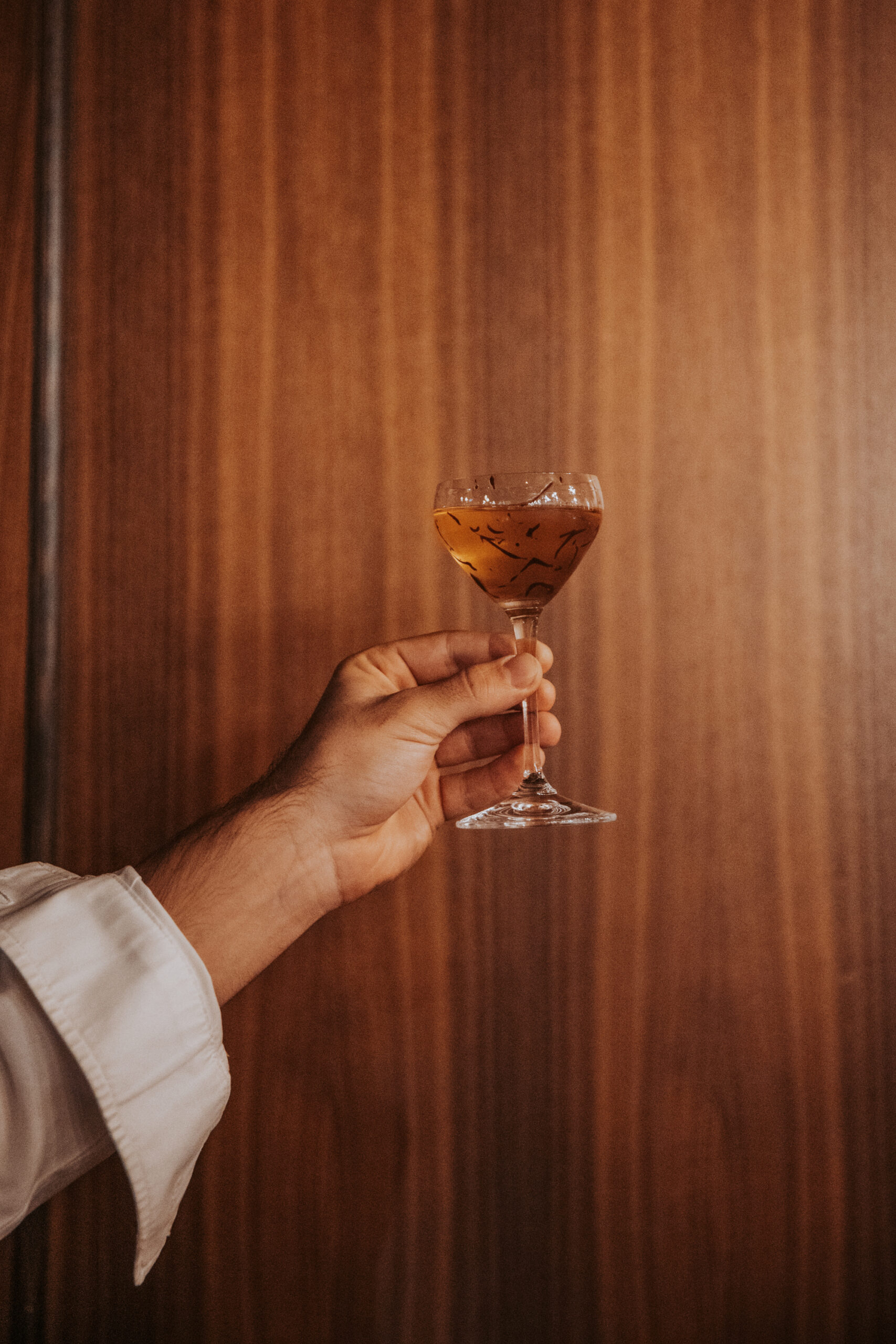 Main tenant un verre à cocktail ambré devant un mur en bois chaleureux