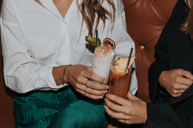 Deux personnes trinquant avec des cocktails artisanaux garnis devant banquette en cuir