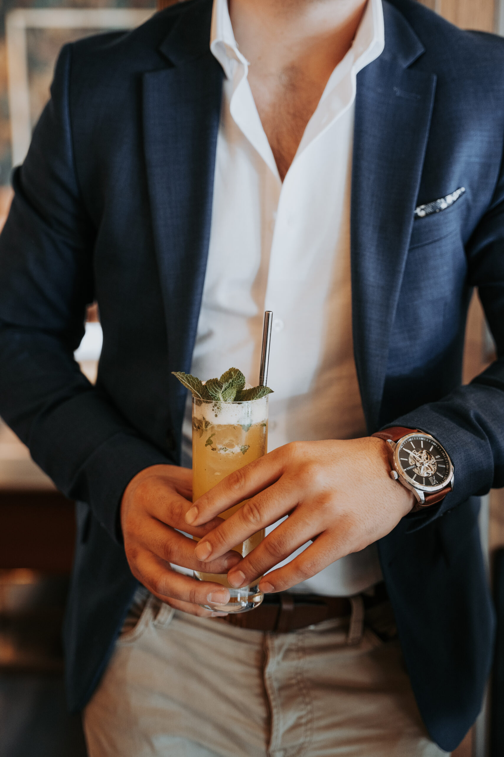 Homme en veston bleu tenant un cocktail à la menthe dans un bar élégant