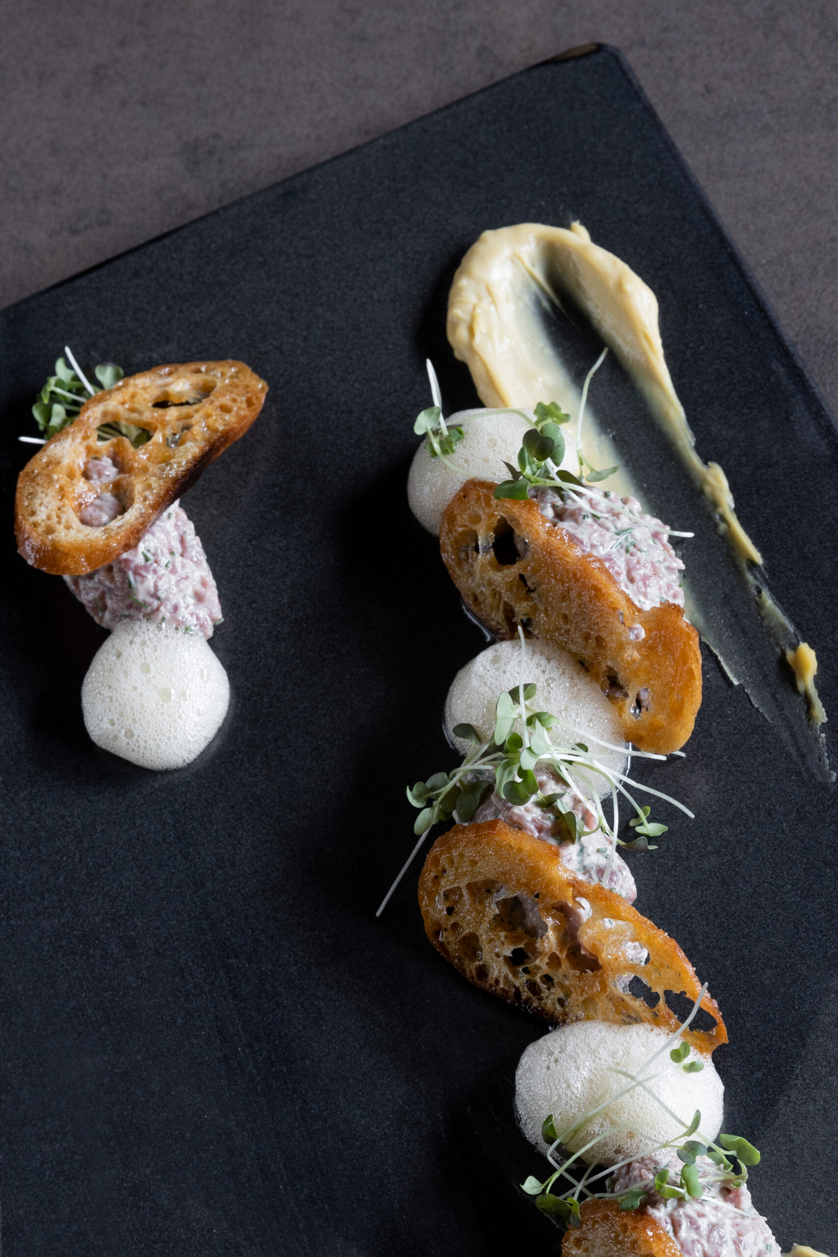 Présentation gastronomique de rillettes sur ardoise noire avec crostinis et micropousses