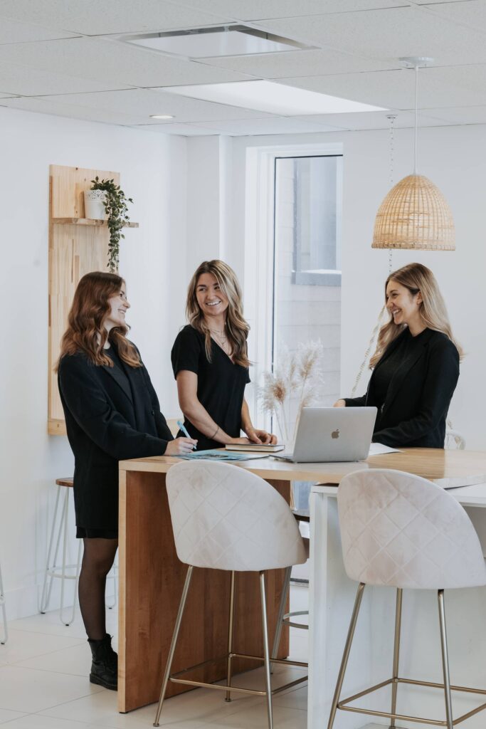 Trois collègues souriantes discutant autour d'un îlot de travail dans les bureaux de Solutions M